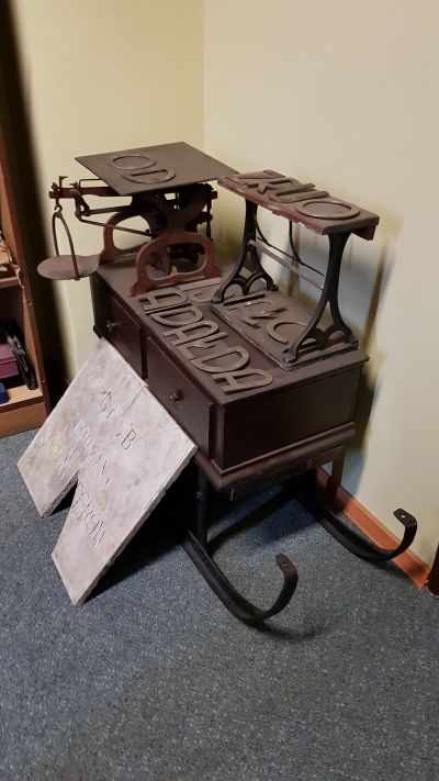 Sanie do przewożenia towar&oacute;w w zimie oraz oparta o nią tablica nagrobna grobu rodziny Schaitter&oacute;w ze Starego Cmentarza. Na saniach umieszczona bardzo dokładna waga, kt&oacute;ra wybijała wartość wagi produktu oraz  litery, z kt&oacute;rych układano napisy określające rodzaj sprzedawanych artykuł&oacute;w w sklepie. Zdjęcie udostępnione przez Pana Grzegorza Dąbrowskiego